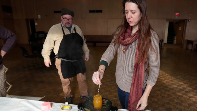 Beekeeper Charlie Koenen watches as Katie Boland dips a wick into beeswax to form a candle at Redeemer Lutheran Church.