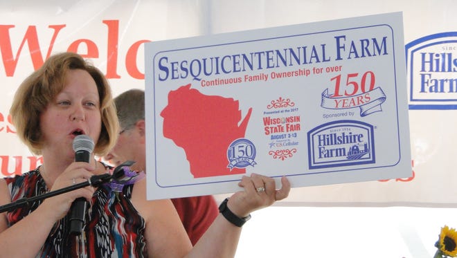 Jyme Buttke, Executive Secretary of Wisconsin Association of Fairs held up the sign the Sesquicentennial Farm families would be receiving at the conclusion of the special breakfast in their honor at Wisconsin State Fair. Century Farm families also received signs.
