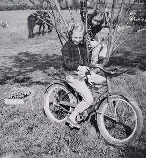 Susan tries out her 'wheels' on her first bike as her sister Karen watches from the tree behind her.